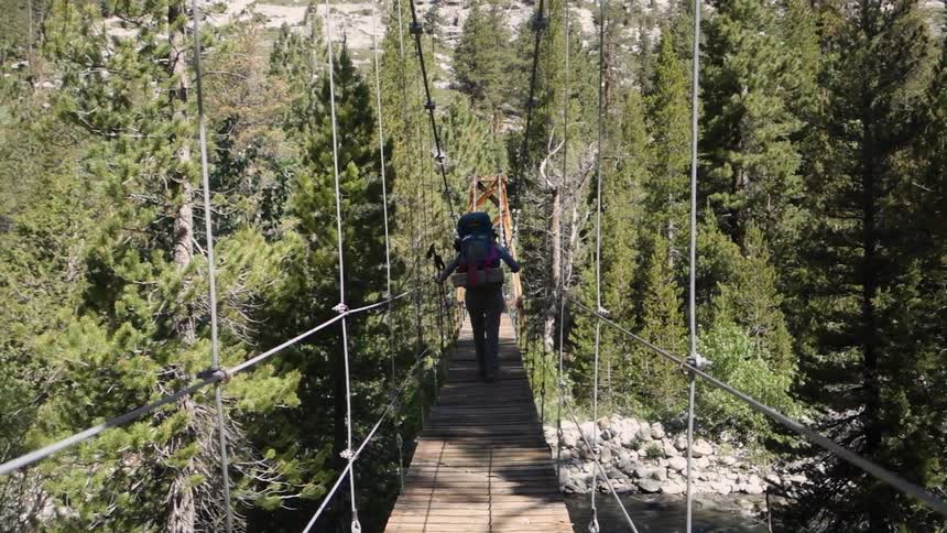 A person walks across a rickety wooden bridge
