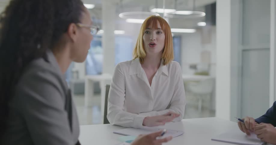 Three women sitting at a desk in an office talking