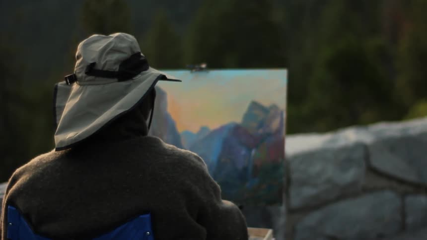 A guy wearing a hat is painting his view of an overlook