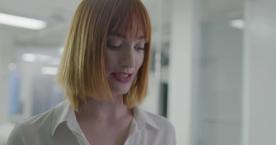 Red haired business woman uses a smartphone and talks to the coworkers in the office