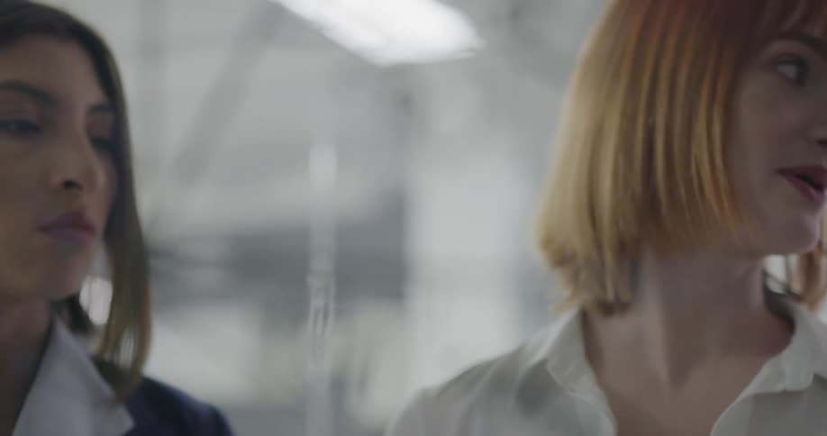 Two women in an office standing in front of a clear board and talking