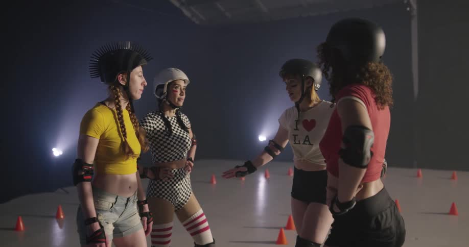 Four women wearing roller skates and protective gear stand in a circle and talk