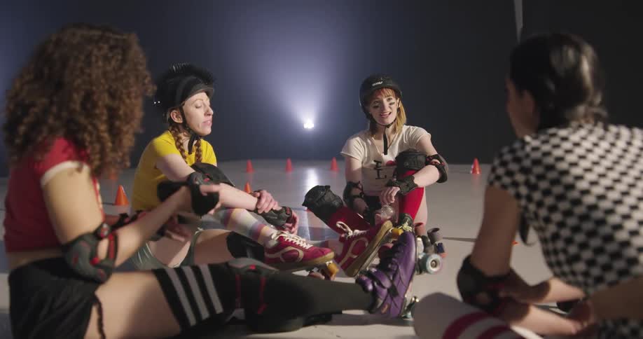Women wearing roller skate gear sitting on the floor talking