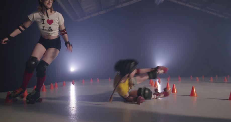 Women roller skating indoors with one woman falling and getting up