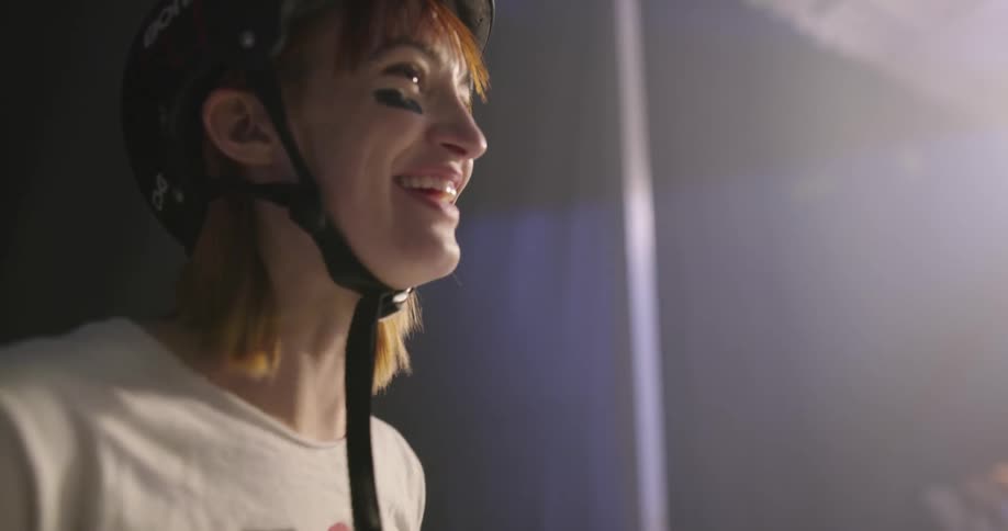 A woman wearing a helmet and wrist guards laughs and talks