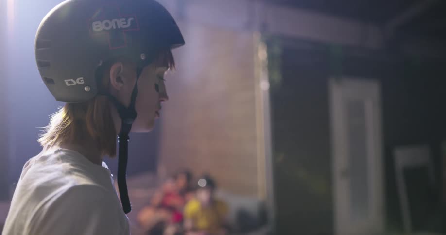 A woman with a helmet standing and drinking bottled water with three women sitting in the background