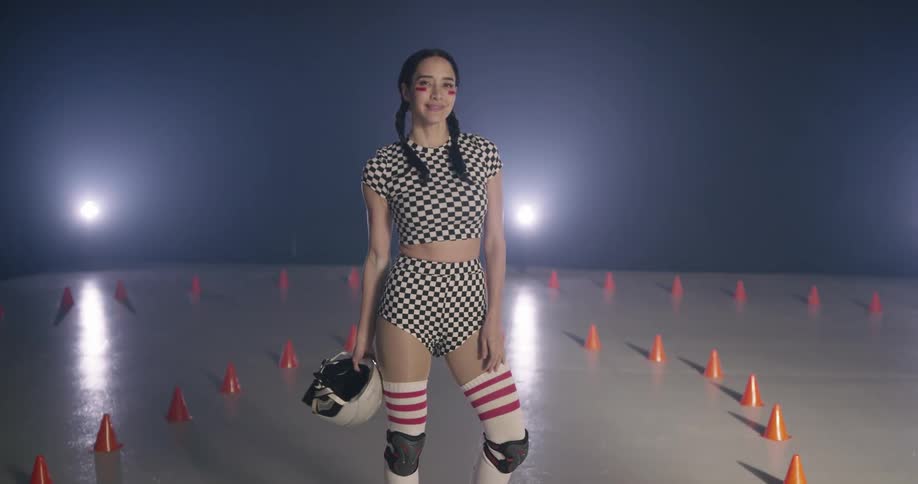 Woman wearing roller skating gear takes off helmet and smiles at camera