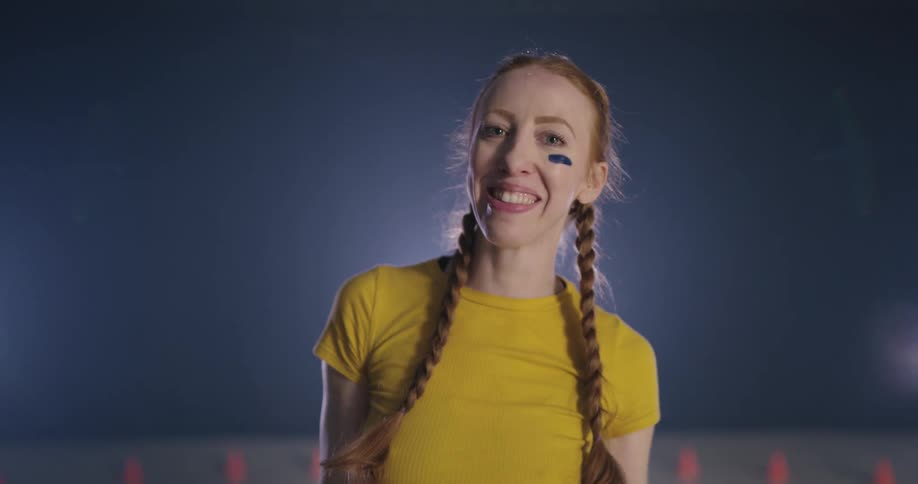 Woman wearing eye black takes off crash helmet and smiles at camera