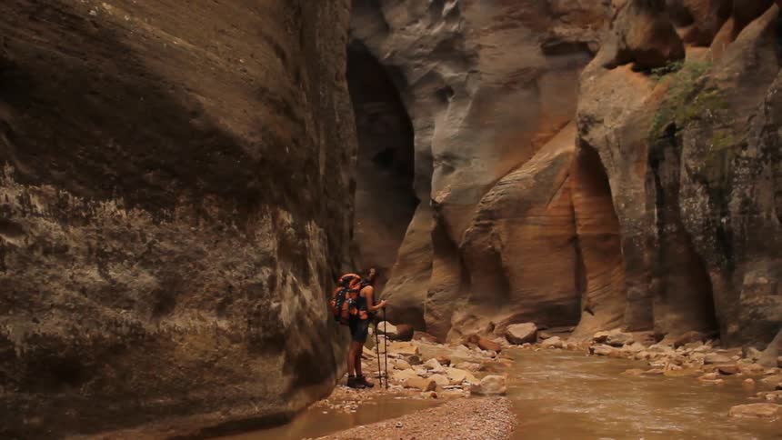 A female hiker walking down a rocky path by a stream of muddy water in the mountains