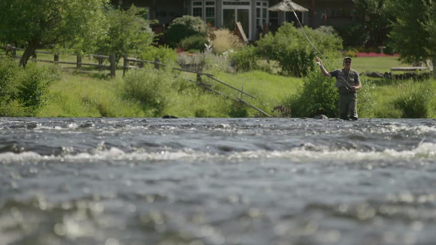 A fisherman stands in a river and casts a fishing line