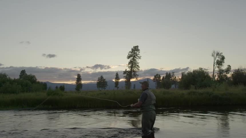 A man fly-fishing in a river on a cloudy evening