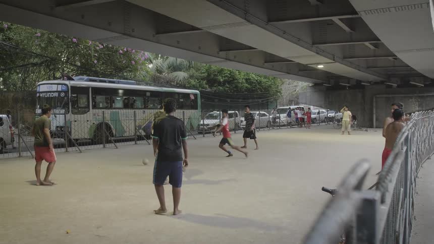 Group of teenagers play football barefoot under a bridge in a city