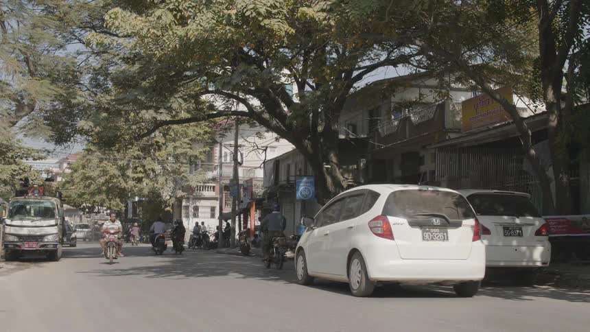 People riding scooters and motorcycles along a road through a neighborhood
