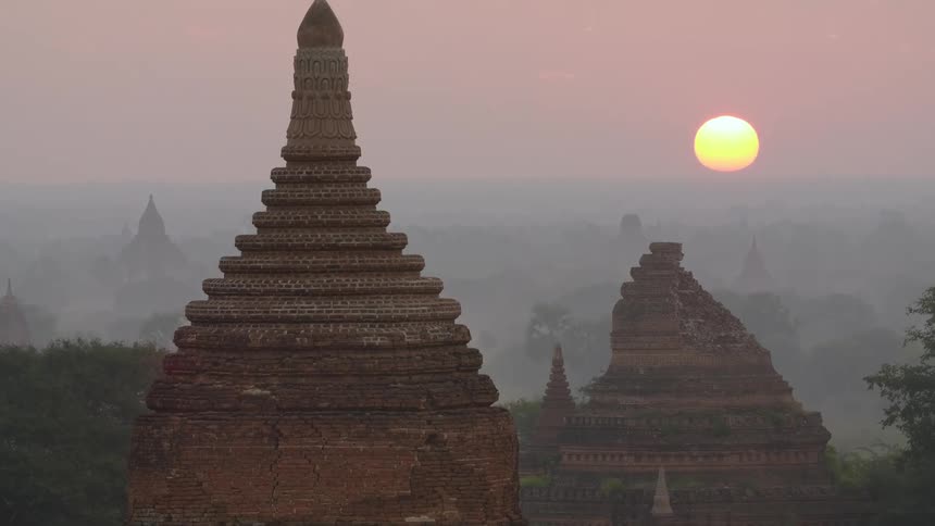 Sun hovers near horizon turning sky red as fog shrouds ornate historical buildings
