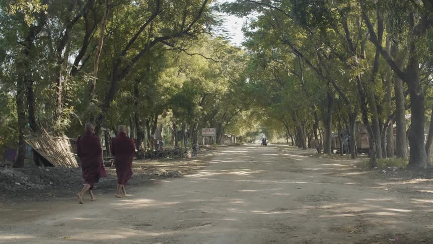 Two people wearing a style of robe walk down a dirt road
