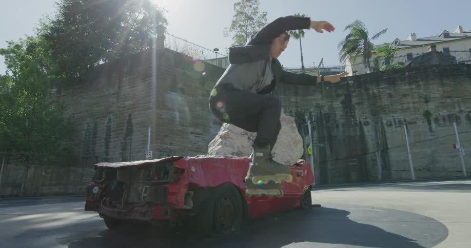 Man moves along the ground using roller skates and jumps over the junk car