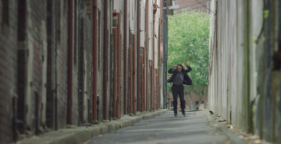 Man wearing a suit rollerblading and jumping through a corridor outdoors
