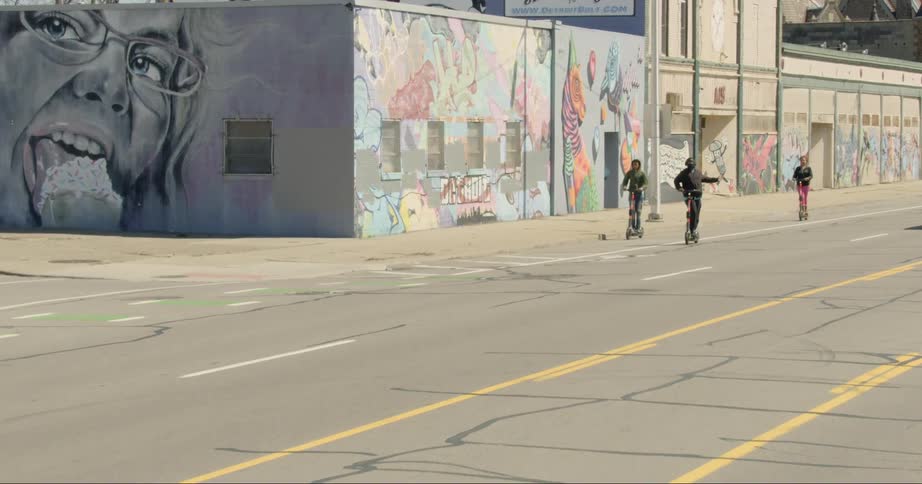 Three friends ride scooters on the road