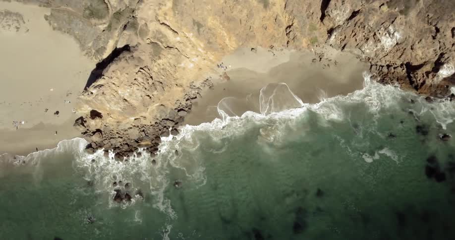 Aerial view of ocean waves crashing against shore on a sunny day