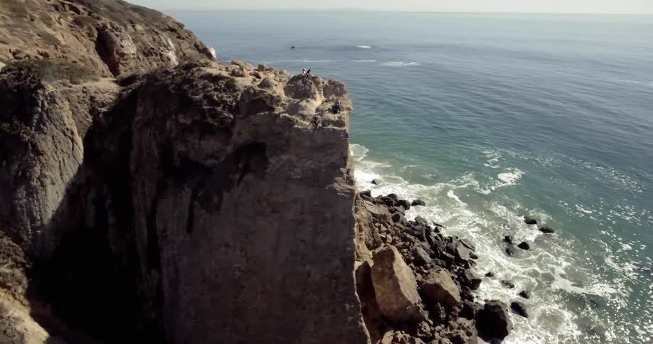 Waves crash onto rocks along the shore below a cliff