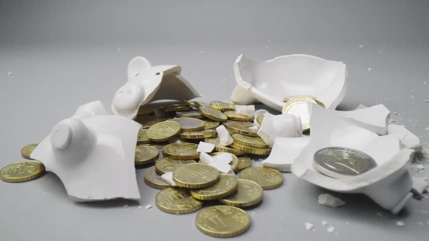 A broken ceramic piggy bank with coins on a table