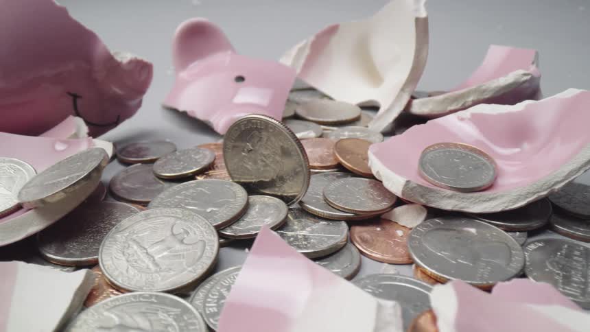 Shattered pink piggy bank and coins laying in a pile