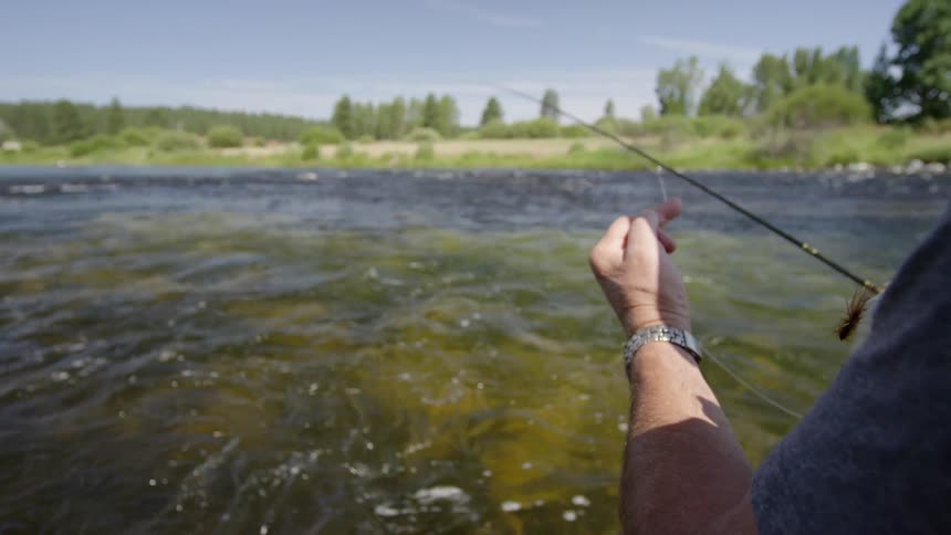 A man fishing in a river tightens the line on his pole