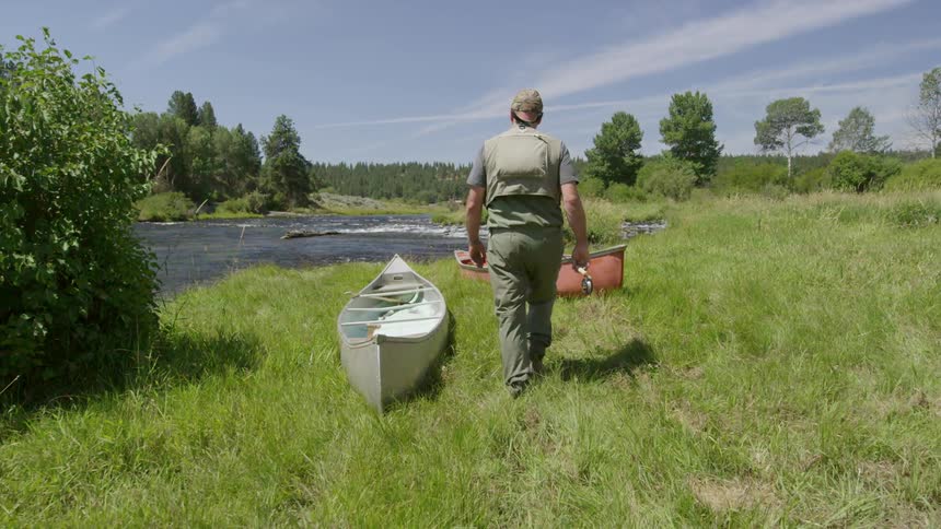 A man carrying a fishing pole walks to a stream
