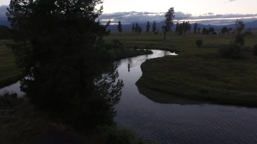 A fisherman stands in a winding river in the wilderness