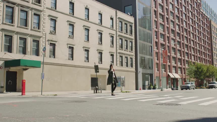A woman crossing a crosswalk in a metropolis while drinking from a cup