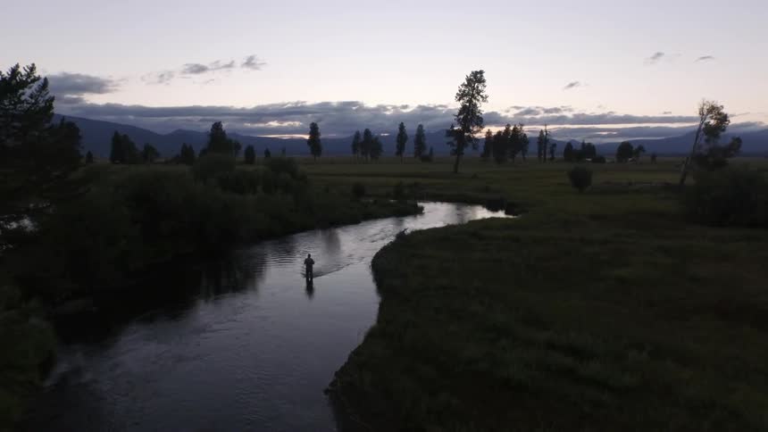 A fisherman stands in a winding river