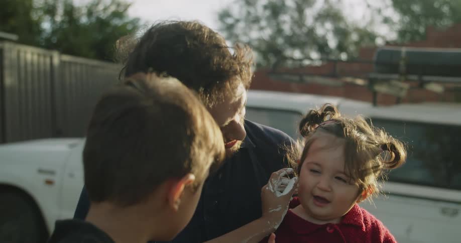 A man holding a little girl in his lap as a boy touches her cheeks