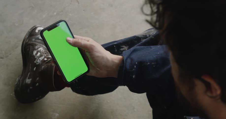 A man in paint spattered clothing swiping the screen of a smartphone with his thumb