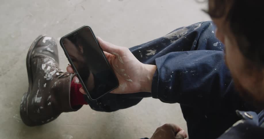 A person in paint splattered clothes looks at a cell phone