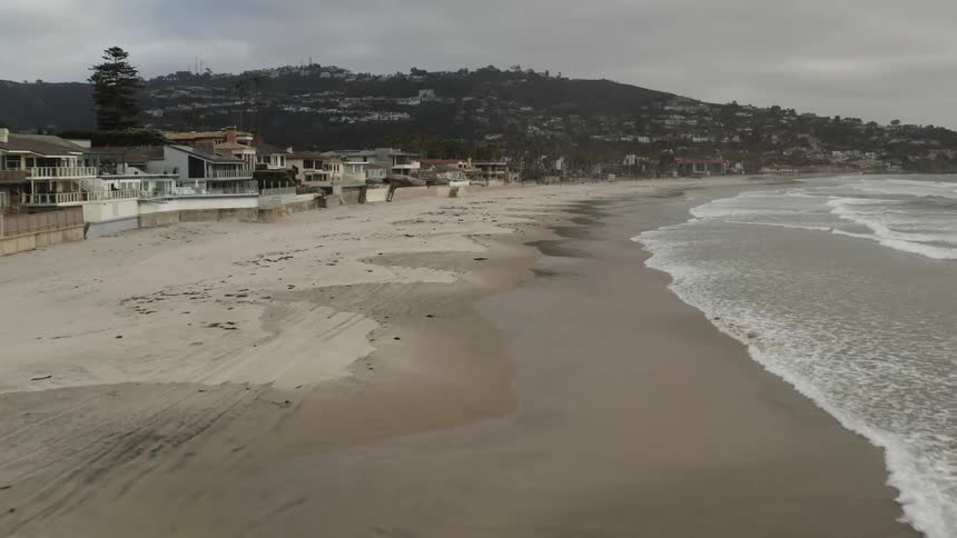 Waves roll in on a beach next to houses