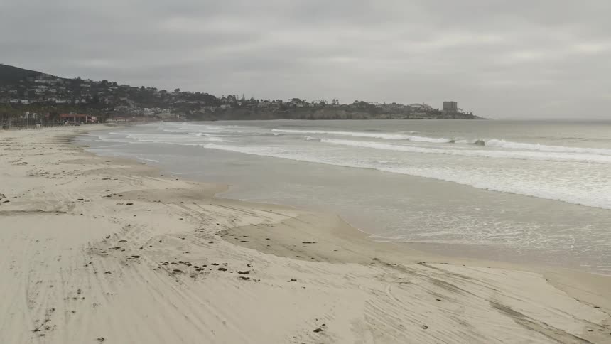 Ocean waves crash against the secluded beach on a cloudy day
