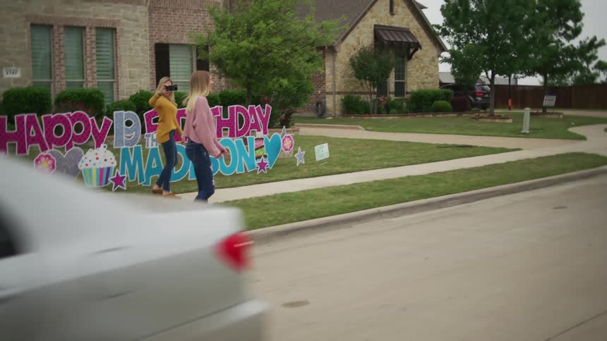 Cars drive by to celebrate girls birthday at a remove while another girl films