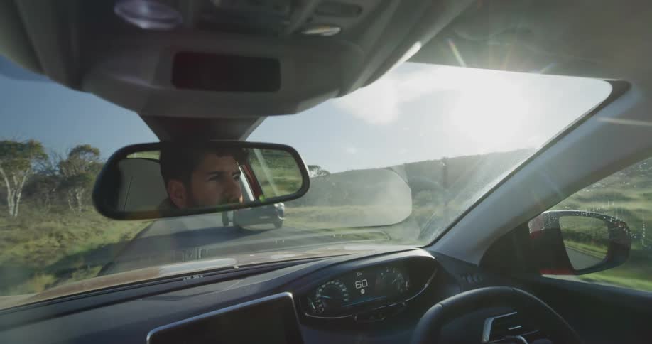 A man driving a car with his reflection in the rearview mirror