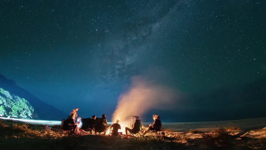 A group of people sit around a fire pit at night