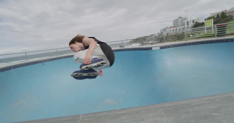 A teenager roller skates in an empty swimming pool in a public park