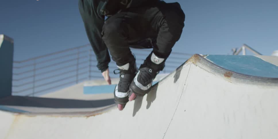 Young man in roller skates does stunts in skate park at day