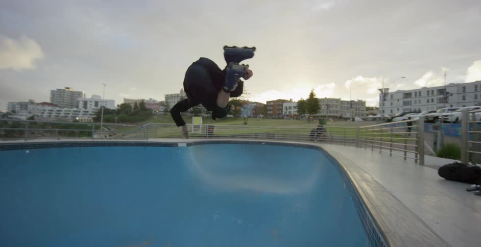 A roller blader skates in an empty pool at a park doing tricks