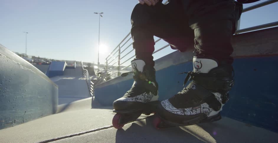 A male wearing roller blades sits on a ledge