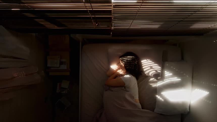 Woman sleeping turns around on bed inside small room