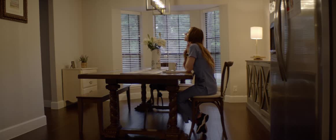 Woman sits alone at dining table with head in hands