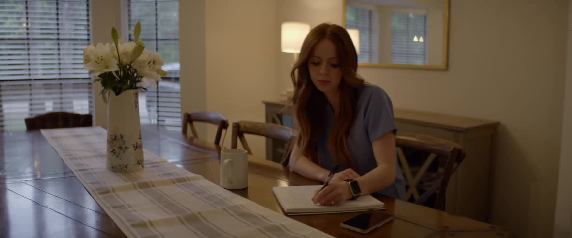A woman sitting at a table writing on a notepad