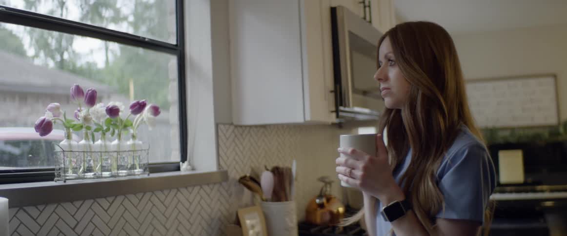 Nurse drinks coffee while standing in the kitchen of her home