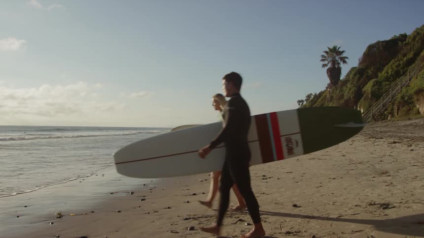 A man and woman carrying surfboards walk to the ocean