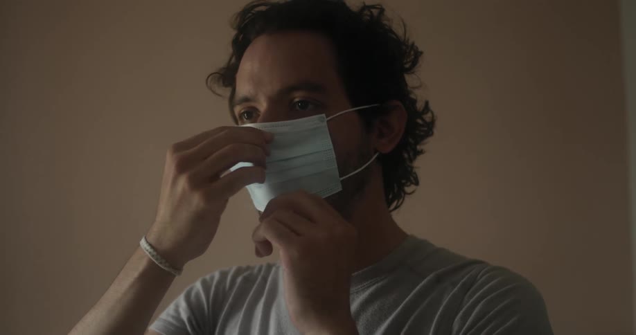 A man putting on a medical face mask before walking off camera