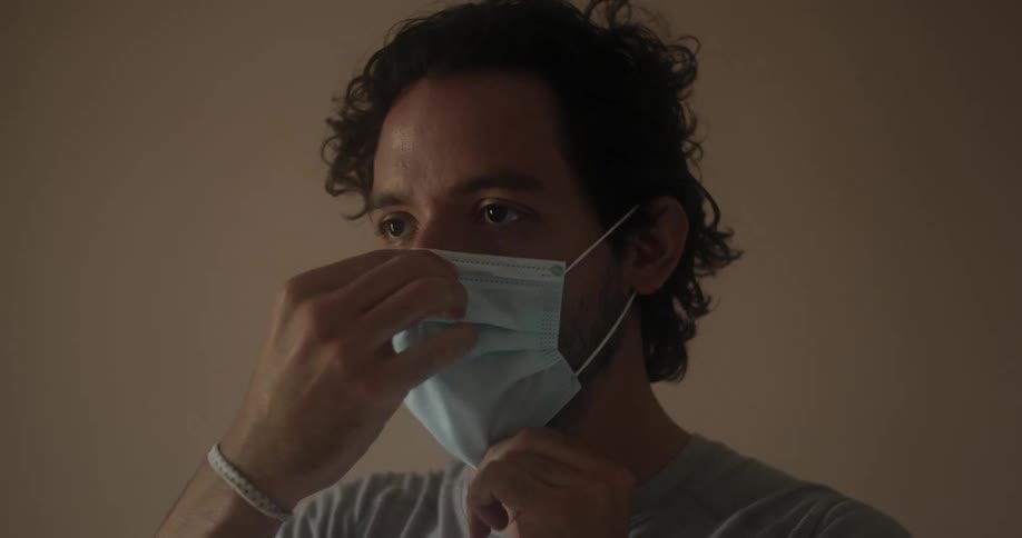 A man places a disposable mask over his nose and mouth and adjusts it to fit correctly